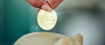 hand putting bitcoin into a piggy bank