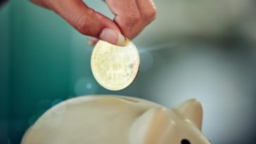hand putting bitcoin into a piggy bank